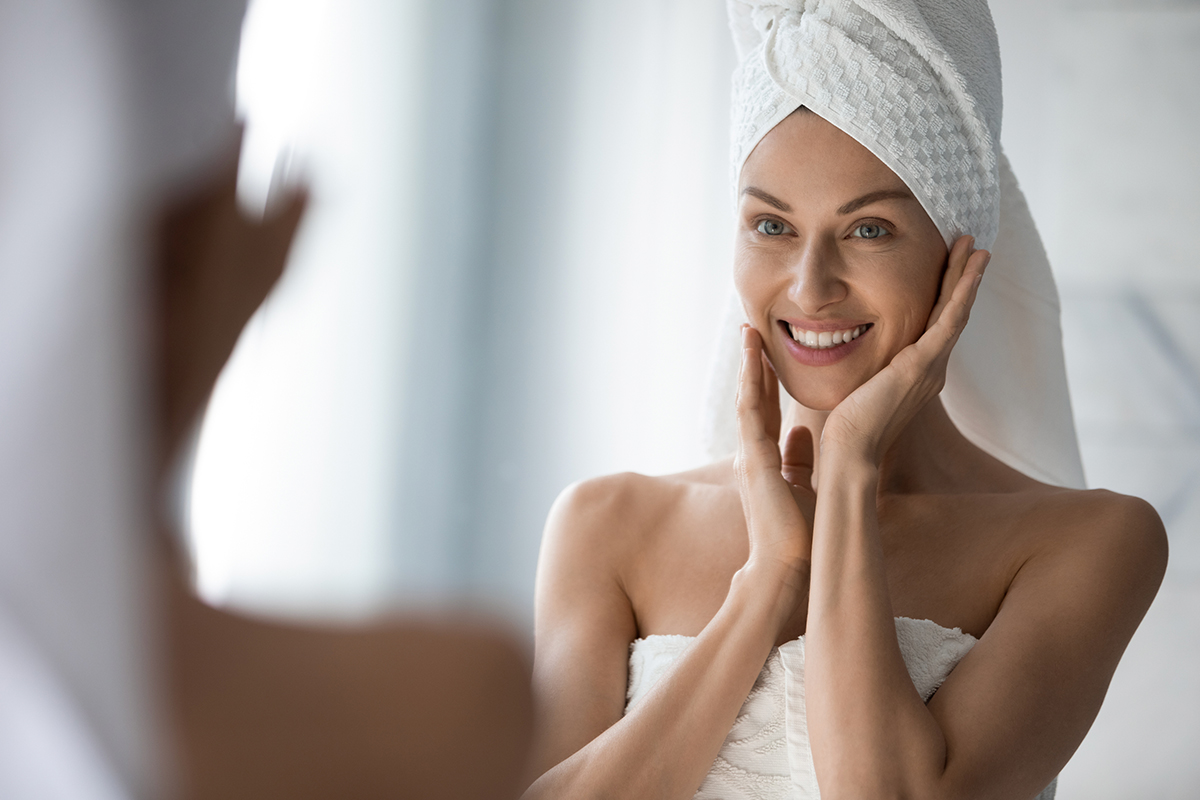 Woman looking in the mirror at her clear face after HydraFacial in Palo Alto.